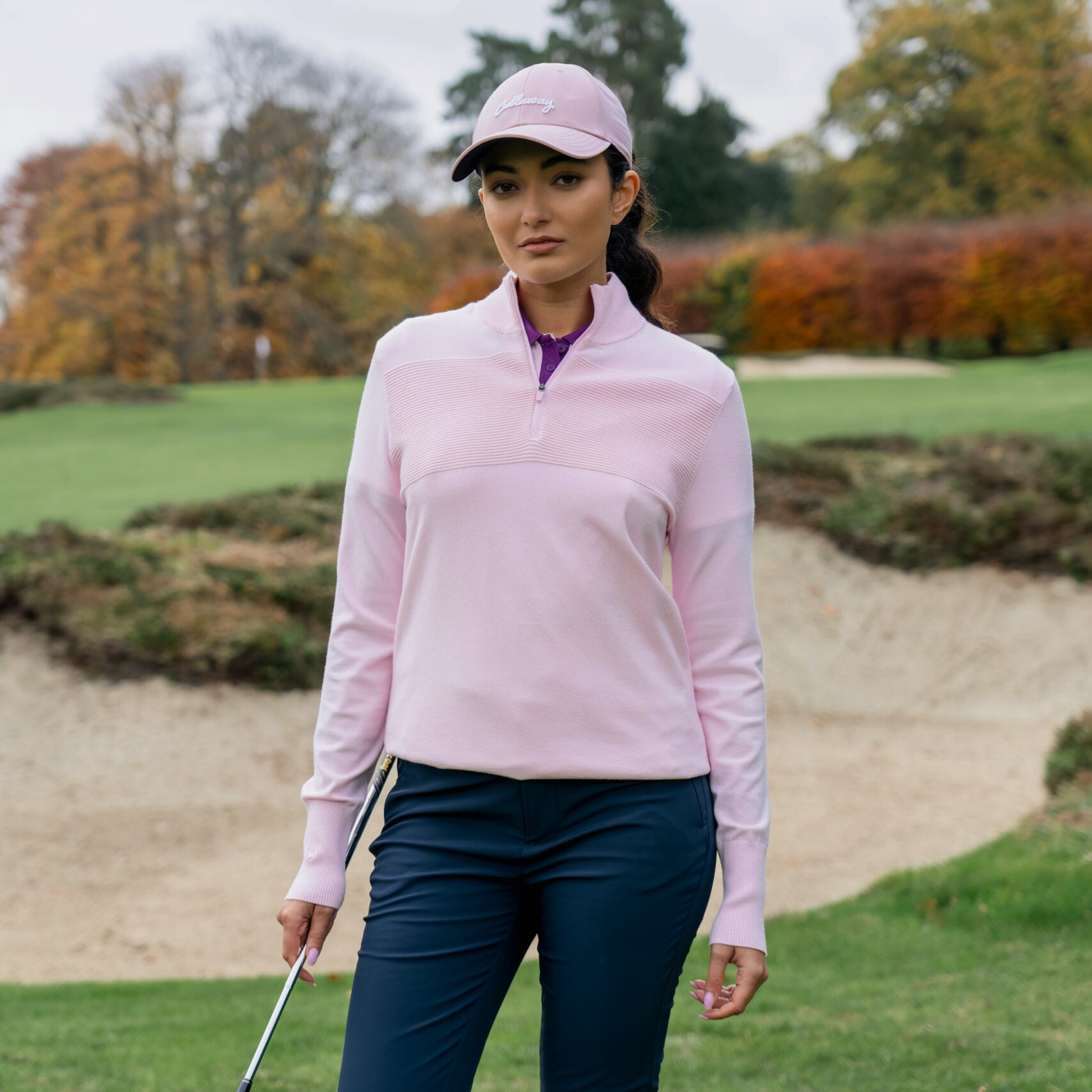 Golfeuse portant le pull zippé à col montant extensible Callaway Soft Stretch en Fleur de Cerisier sur le parcours de golf